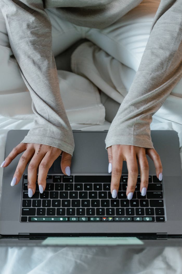 gallery-4 Close-up view of a woman's hands typing on a laptop keyboard while sitting comfortably indoors.